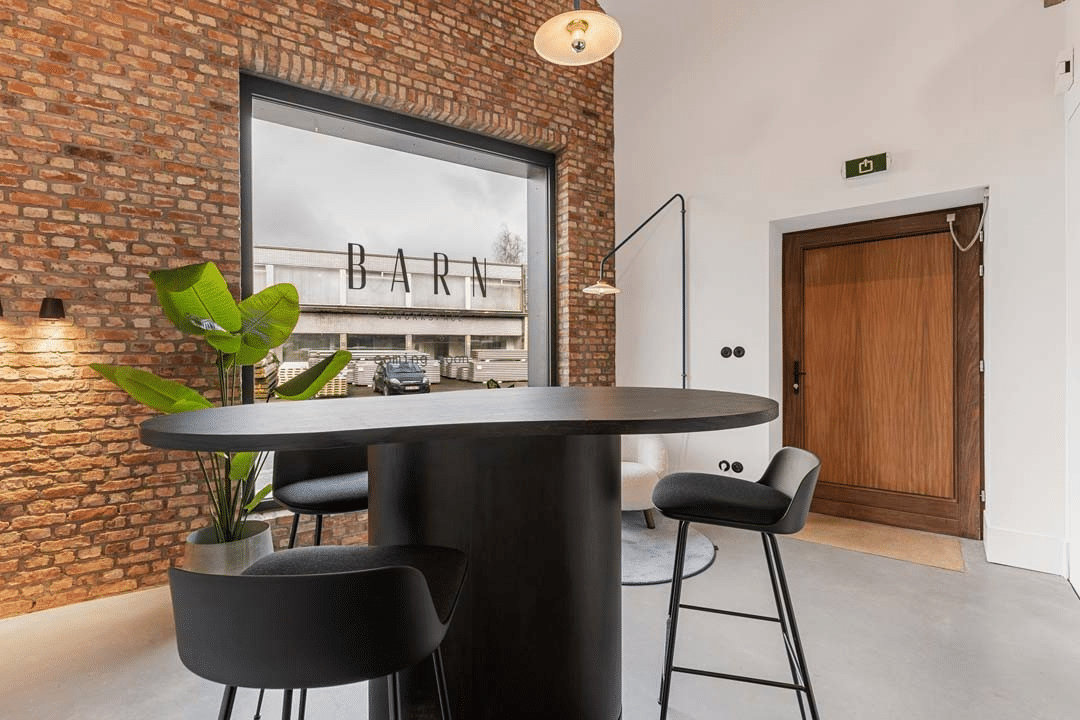 Zone d'accueil avec table haute et mur en briques chez Barn Coworking, aménagée par Buro Project