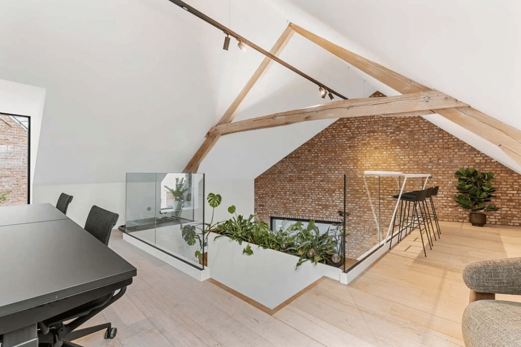 Espace de coworking ouvert sous des poutres en bois avec des places assises, des accents verts et des matériaux durables, conçu par Buro Project