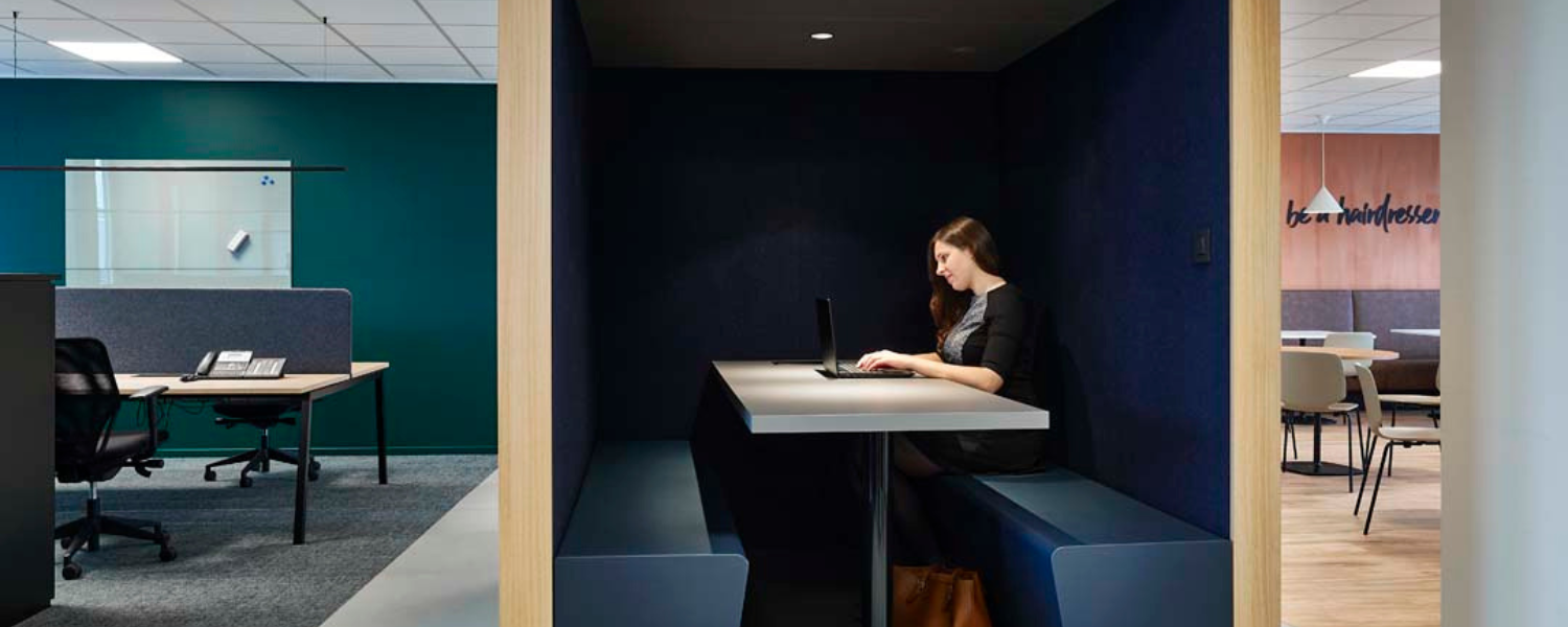 Une femme travaille de manière concentrée dans une cabine acoustique au sein d’un bureau paysager pour plus de calme et de focus