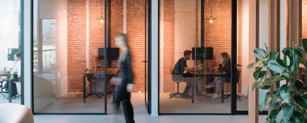 Moderne kantoorruimte met glazen vergaderruimtes, flexibele werkplekken en medewerkers die samenwerken in een slimme werkomgeving.