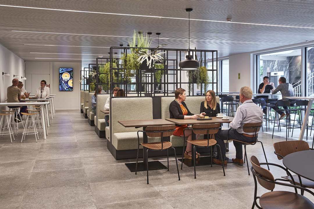 Levendige lunchruimte met groene plantenwanden en comfortabele ziteilanden waar collega's samenkomen