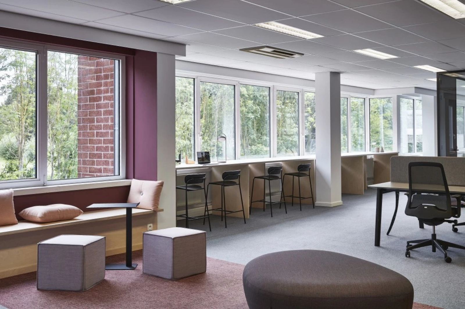 Espace de bureau lumineux avec des tabourets de bar compacts le long de la fenêtre et des éléments d’assise modulaires qui maintiennent la fonctionnalité de la pièce sans la surcharger.