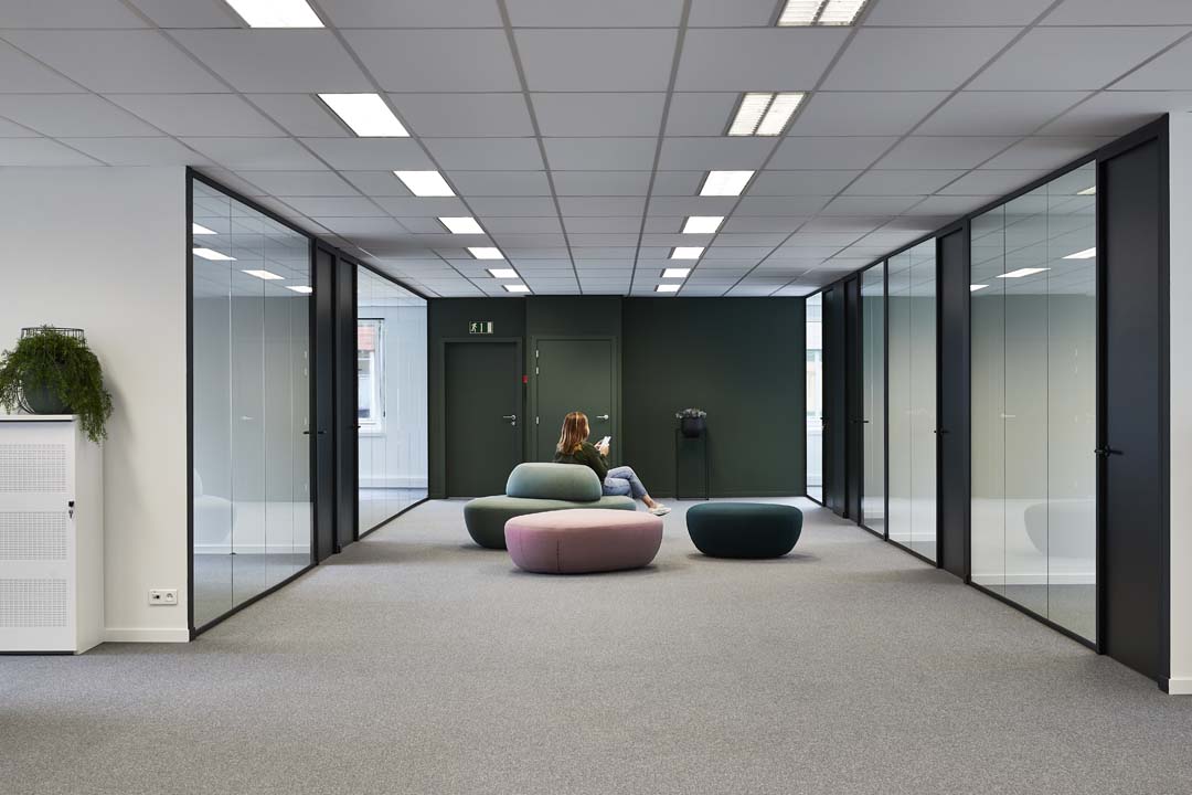 Espace de bureau ouvert avec tapis, poufs souples et parois vitrées qui limitent la réverbération sans perdre l’ouverture.
