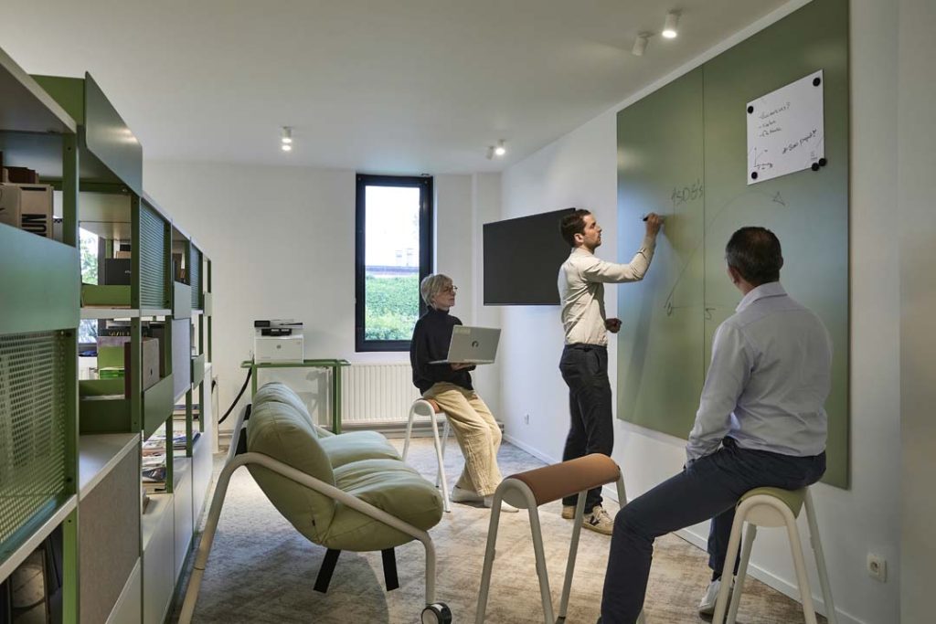 Team brainstormt met laptop en whiteboard in een creatieve overlegzone.
